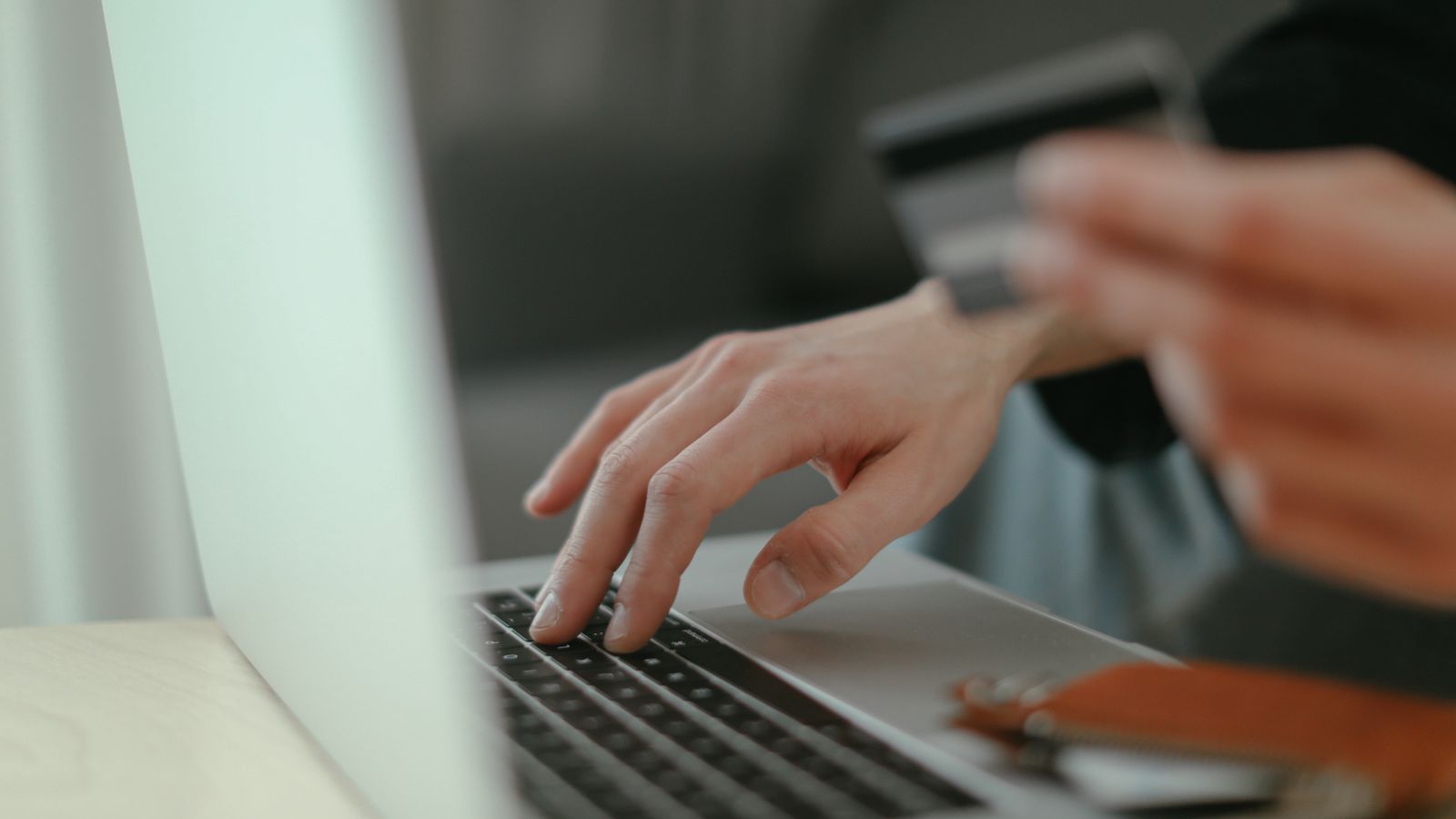 Dłoń trzymająca kartę płatniczą przy laptopie